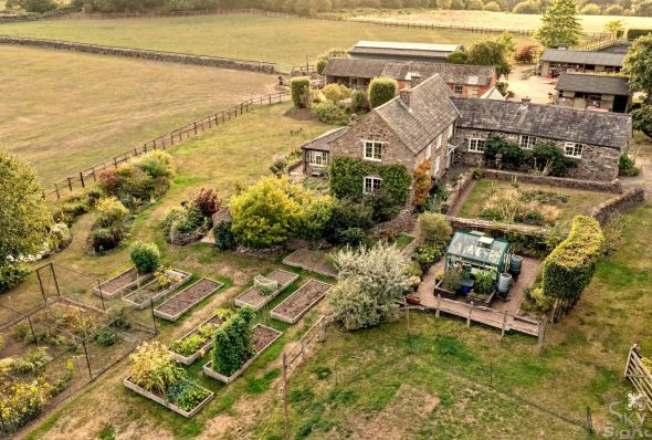 A drone view of a beautiful cottage with surrounding garden and fields